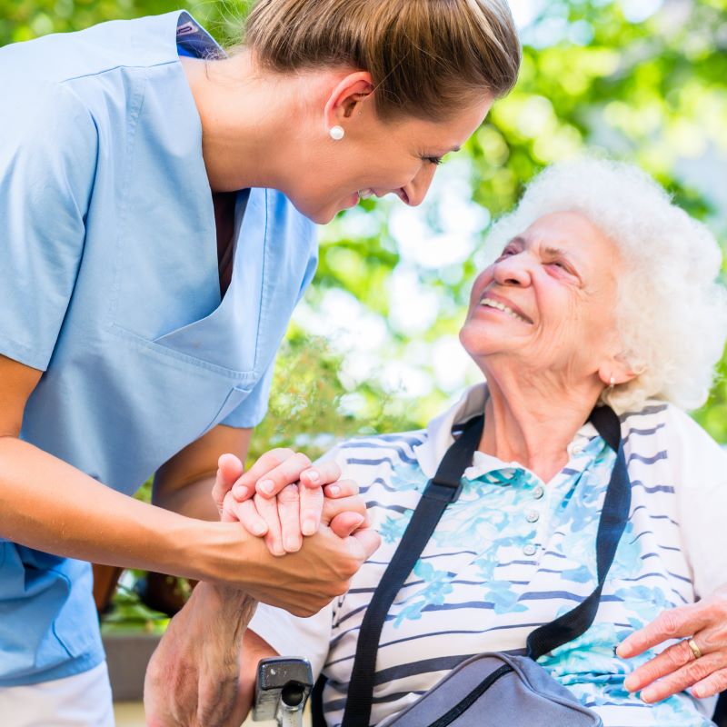 Nurse holding hand of senior person in a wheelchair.