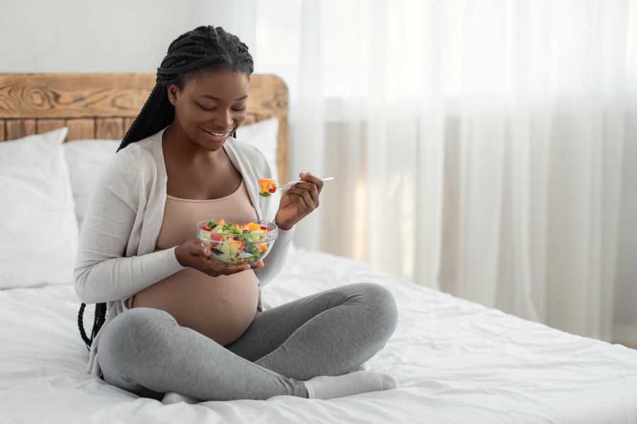 Pregnant woman on bed eating bowl of salad