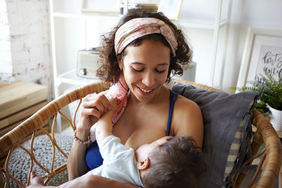 A woman smiles down at her baby while breastfeeding in wicker chair. A woman smiles down at her baby while breastfeeding in wicker chair.