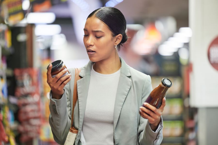woman grocery shopping holds two products deciding which to buy