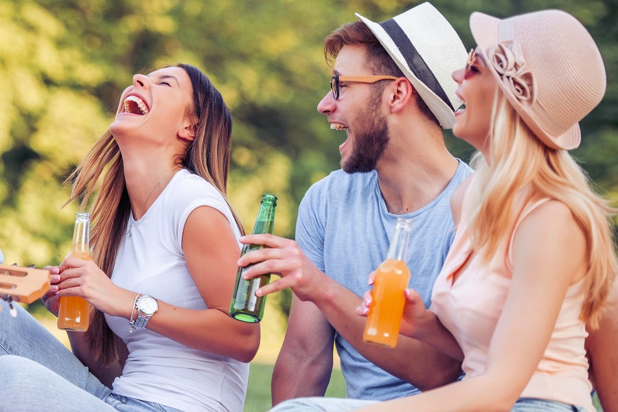 one young man and two women in the park with beer laughing one young man and two women in the park with beer laughing