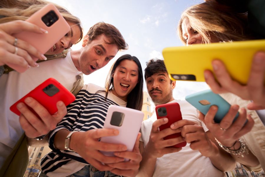 Diverse group young people in circle staring in surprise at cell phone screen Diverse group young people in circle staring in surprise at cell phone screen