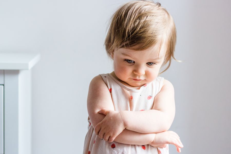A sad looking toddler crosses her arms and looks to the ground. A sad looking toddler crosses her arms and looks to the ground.
