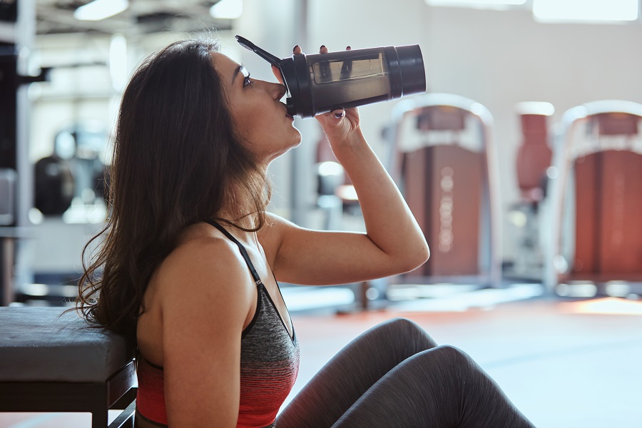 Young active woman taking a break in the gym and drinking protein shake