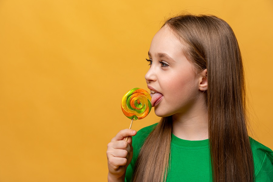 A happy little girl in green tshirt eating a lollipop caramel on a stick
