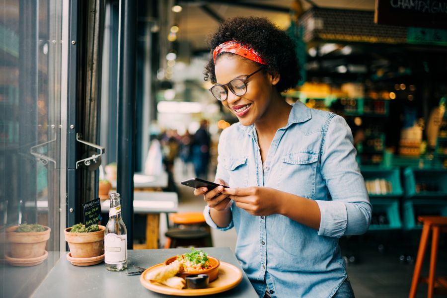 A woman smiles while taking a picture of her food in a resteraunt.
