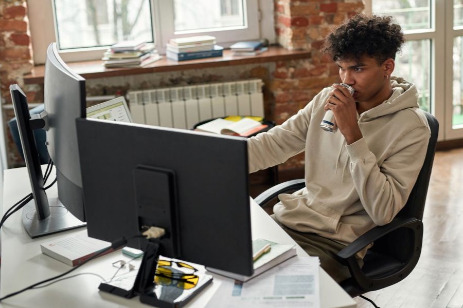 A student studies and works at his computer while sipping from a non-descript can.