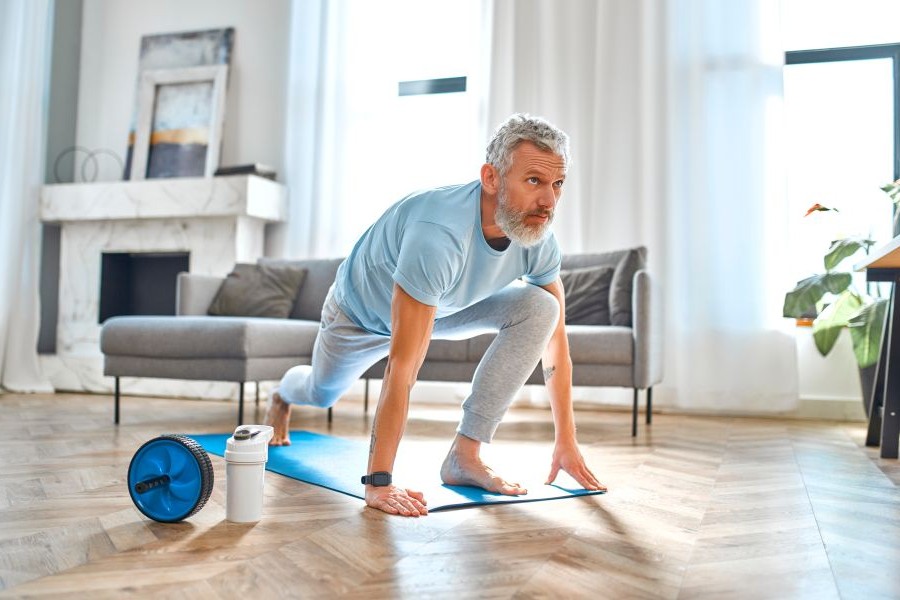 An older man exercising on a yoga mat in a brightly lit room.