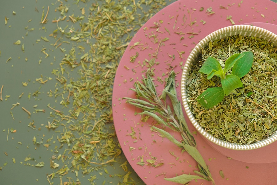 Dry and fresh green stevia in a round cup on a pink pedestal on green background Dry and fresh green stevia in a round cup on a pink pedestal on green background
