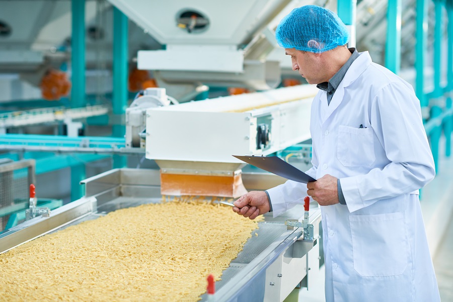 factory worker doing production quality inspection in food industry holding clipboard standing by conveyor belt