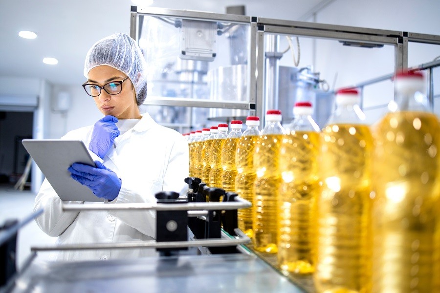 FormattedPicture a female factory worker standing next to oils in bottles and looking at data on a tablet