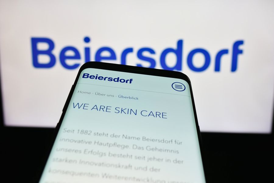 Beiersdorf in the background with a phone in front with "we are skin care" written on it. Beiersdorf in the background with a phone in front with "we are skin care" written on it.