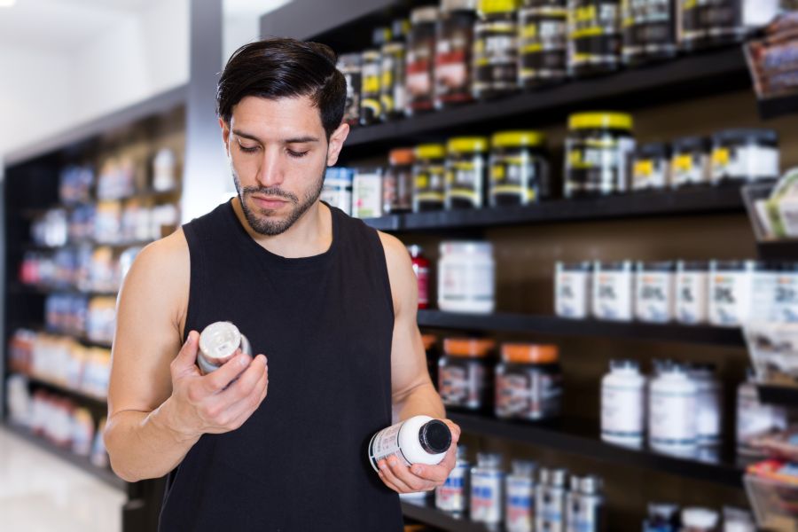 A man stands in a store aisle trying to choose between two different supplements.