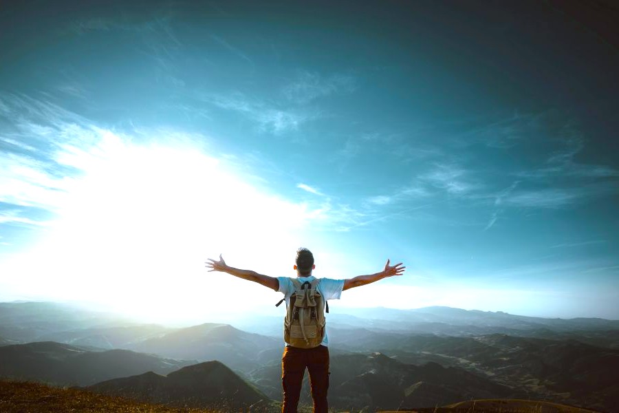 Image A man spreading his arms to the sky after having hiked to the top of a mountain.