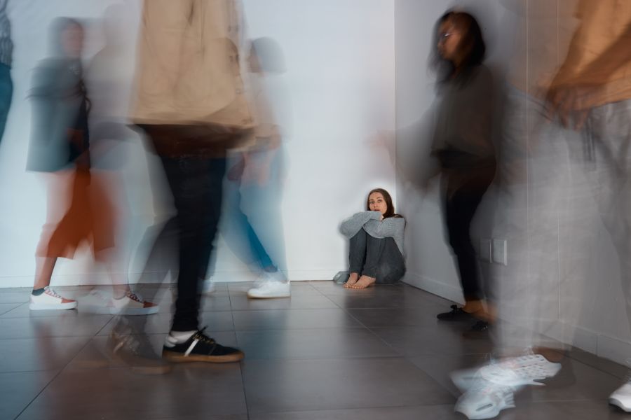 A girl sitting in a corner while people walk around her.
