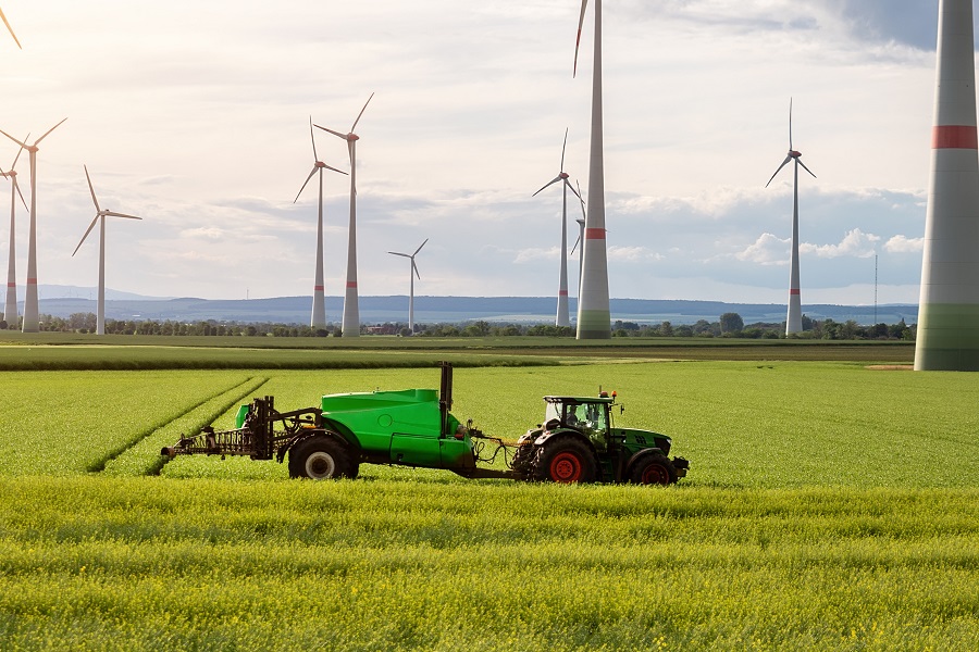 tractor in a huge green field with windmills in the background