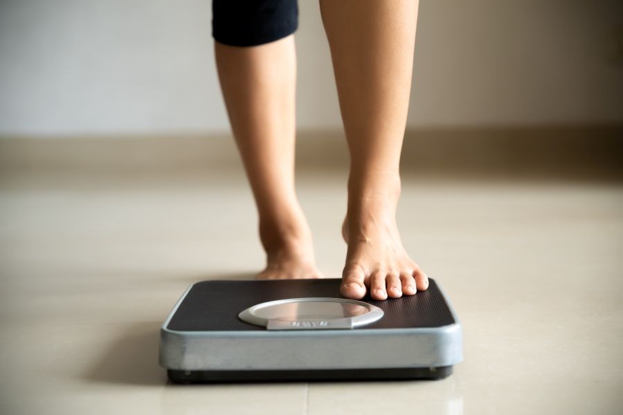 A woman's legs and feet with one stepping on a scale.