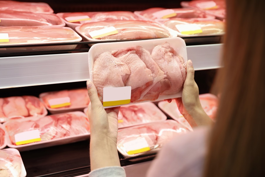 a woman’s hand holding packed fresh chicken in supermarket