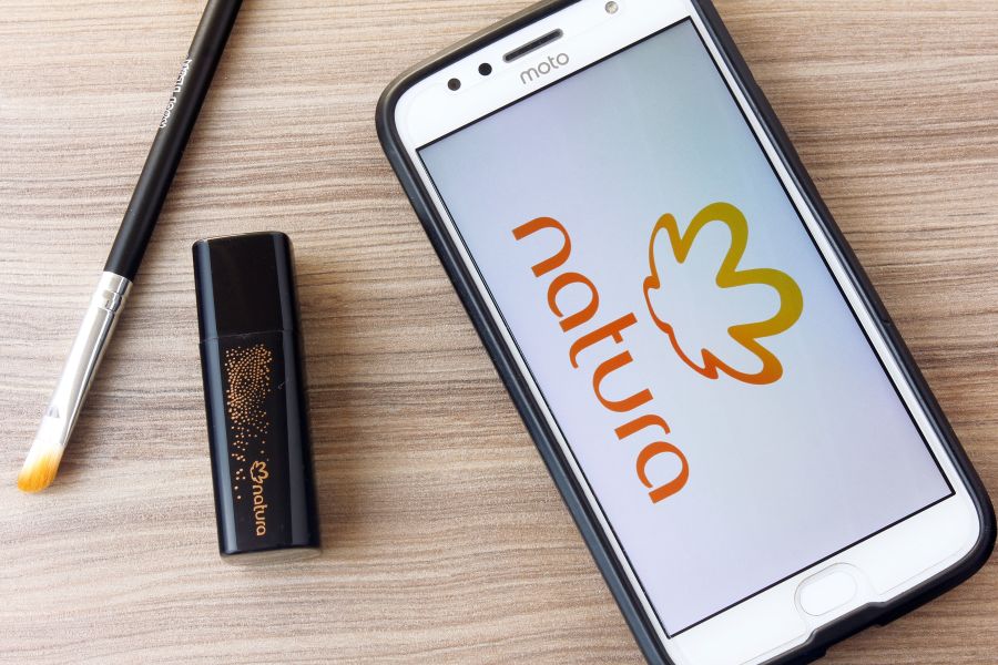 A phone with the Natura logo on it next to a makeup brush and lip product.