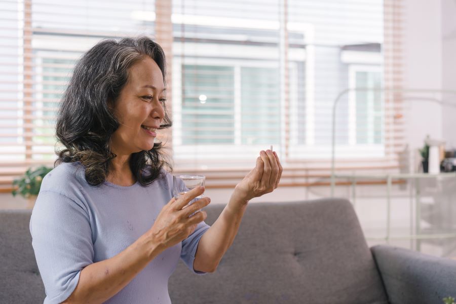 Close-up of a happy senior lady holding a glass of water and taking a pill.