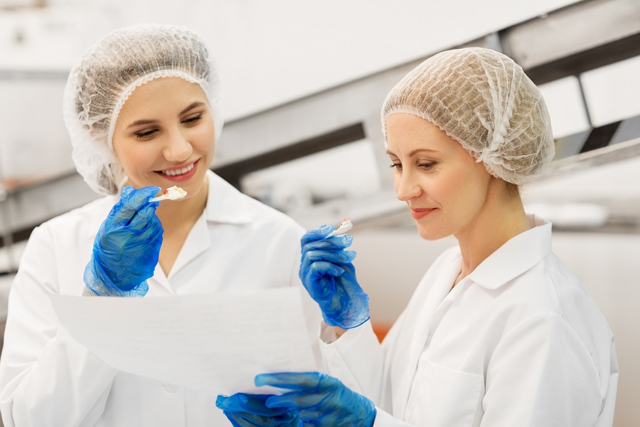 Image happy women technologists tasting ice cream in factory