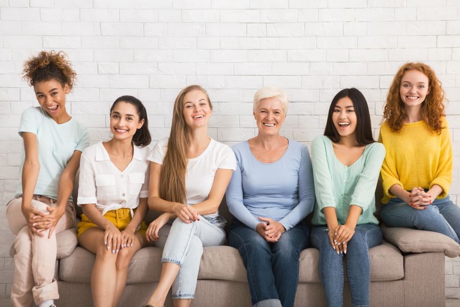 Several happy women of all ages and demographics sitting on a couch and laughing. Several happy women of all ages and demographics sitting on a couch and laughing.