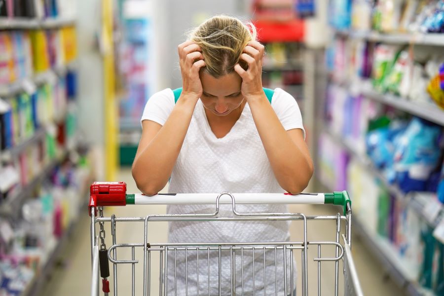 Upset woman holds head leaning on trolley in a supermarket Upset woman holds head leaning on trolley in a supermarket