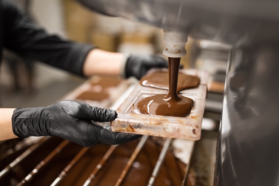 a hand wearing black gloves filling chocolate in mold