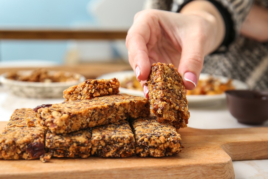 Image woman's hand picking up a granola bar among many kept on a wooden board