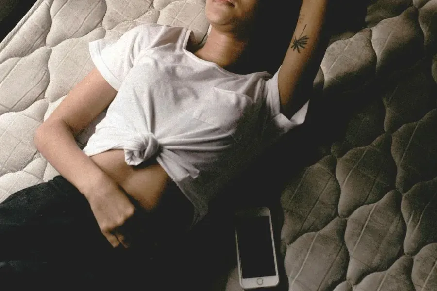 A woman lying in bed in pain with her phone next to her.