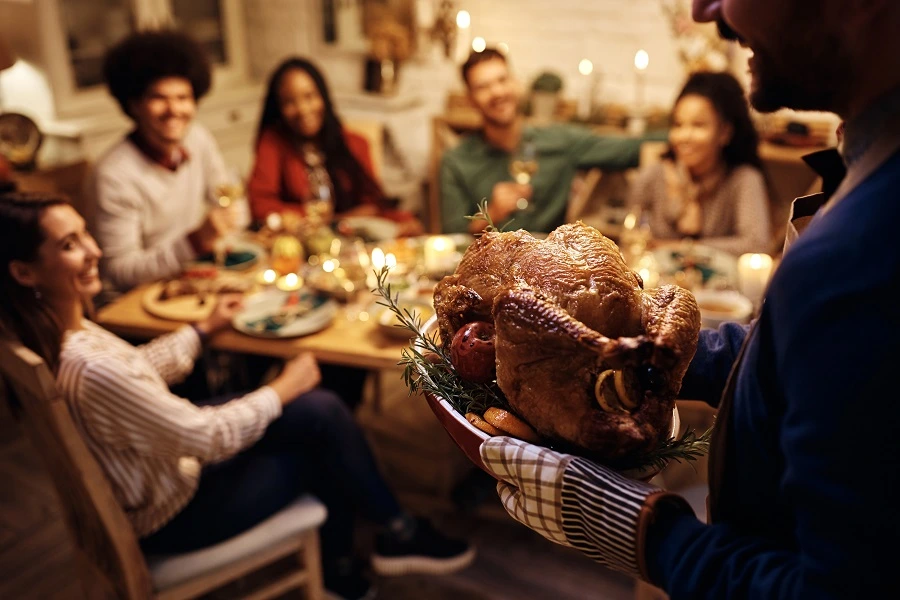 man's hand holding roasted turkey with friends waiting at dinner table man's hand holding roasted turkey with friends waiting at dinner table