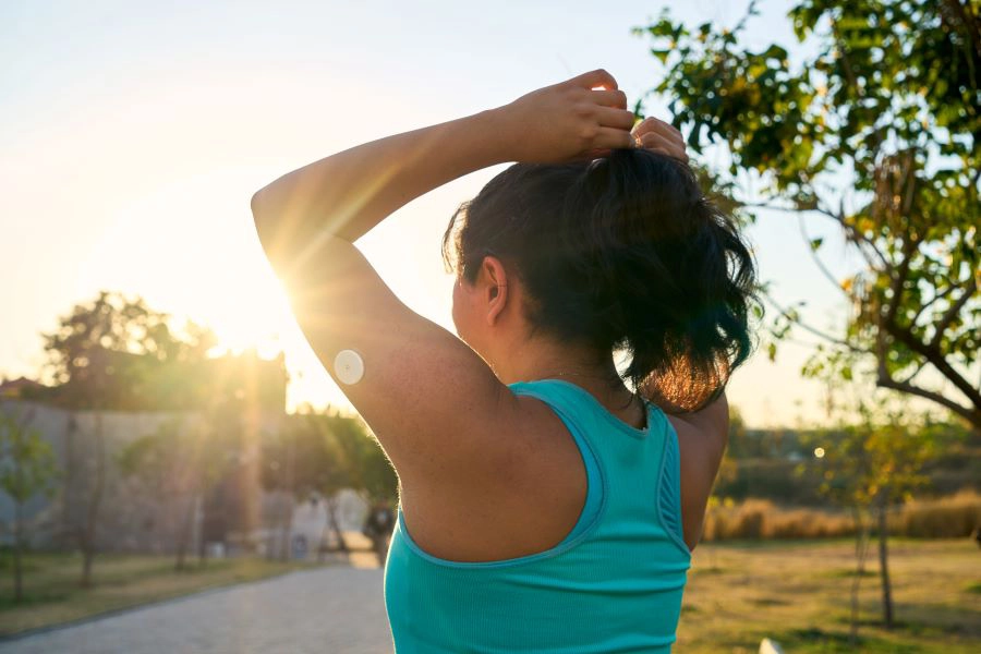 Young Latin sportswoman tying hair with glucose sensor or monitor at sunset in park.