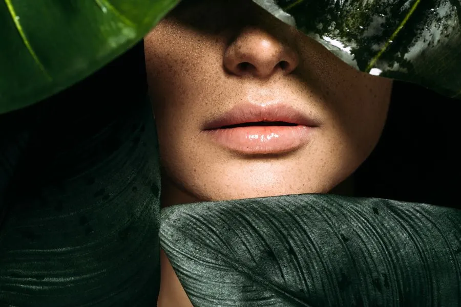 The bottom of a woman's face with plants in front of it. The bottom of a woman's face with plants in front of it.