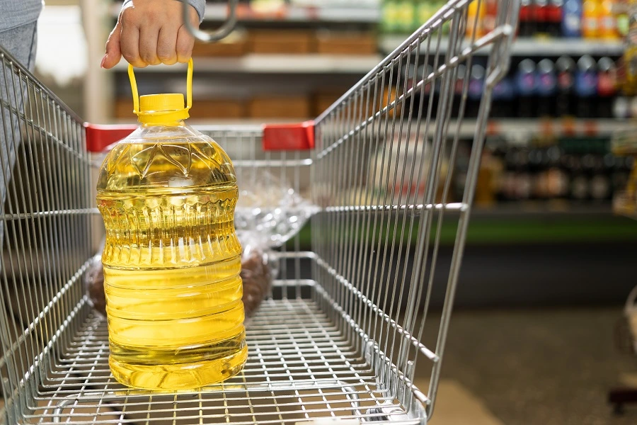 woman's hand putting bottle of yellow oil in shopping cart woman's hand putting bottle of yellow oil in shopping cart