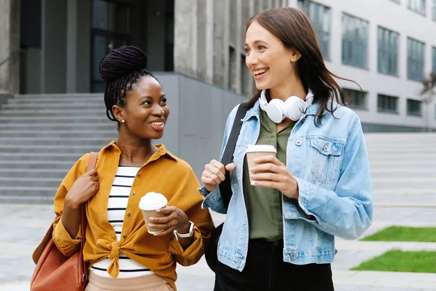 two women walking with coffee cups two women walking with coffee cups