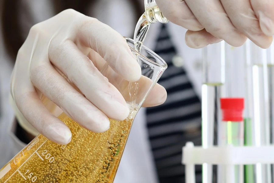 female hand in white gloves pours beer from bottle into flask in lab