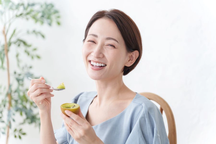 Happy woman eats gold kiwi with spoon Happy woman eats gold kiwi with spoon