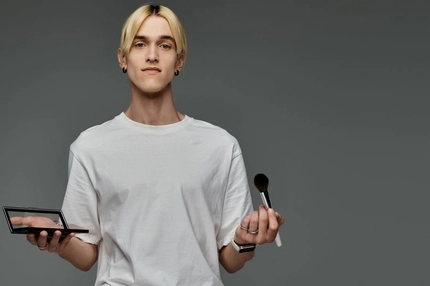 Image A man holding a makeup palette and a makeup brush.