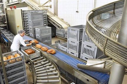 Image woman in white shirt and pants in bakery factory with bread on conveyor belt