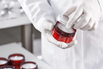 Hands wearing gloves opening a pot of cream.