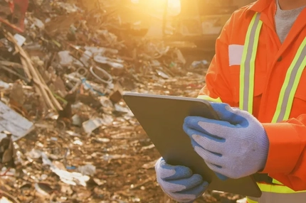 A person holding a tablet in front of a pile of trash