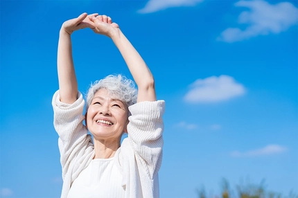 Old happy woman stretches arms in the air outdoors