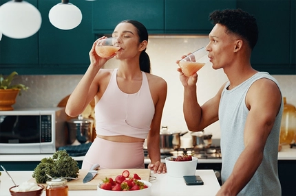 Image Man and woman in gym gear drinking juice in kitchen