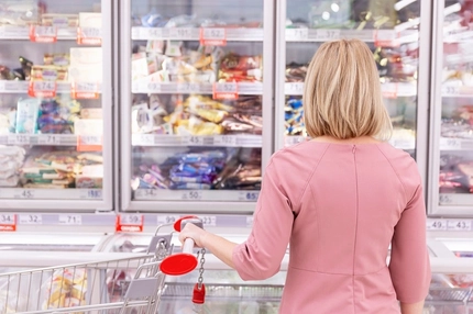 Image woman in pink sweater looking at frozen food section in supermarket