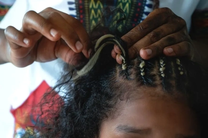 Hands braiding a young girls hair with blonde extensions.