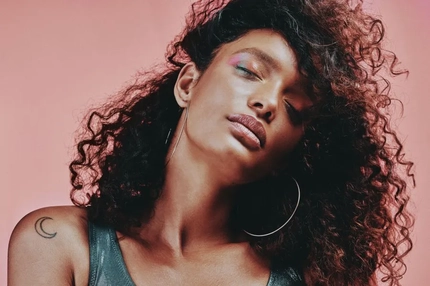 A woman with curly hair tilting her head with her eyes closed.