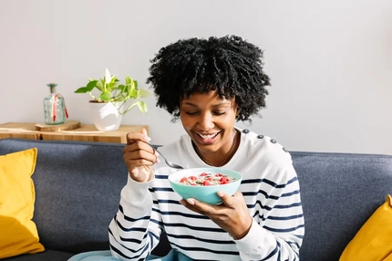 A woman eating fruit-filled yogurt on a couch.
