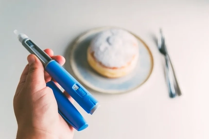 A person holding a GLP-1 medication injector in front of a donut.
