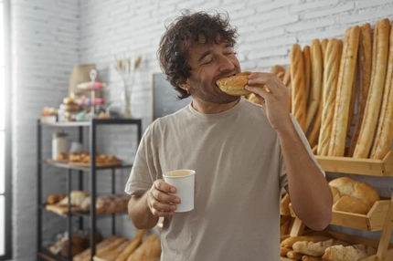 A man eating a donut and drinking a coffee in a bakery.