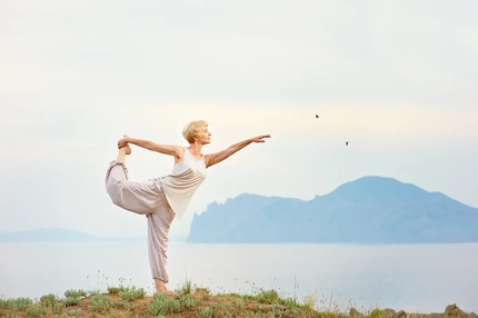 Senior woman doing yoga exercises by ocean with island in background